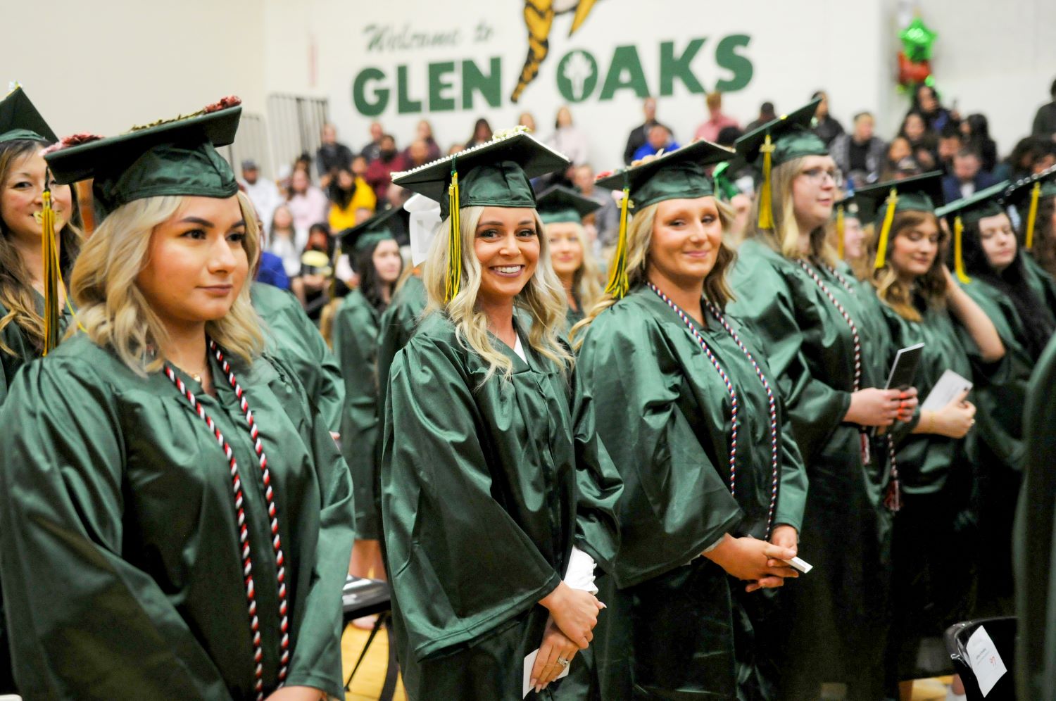 Graduation ceremony with female graduates wearing green caps and gowns looking into the camera