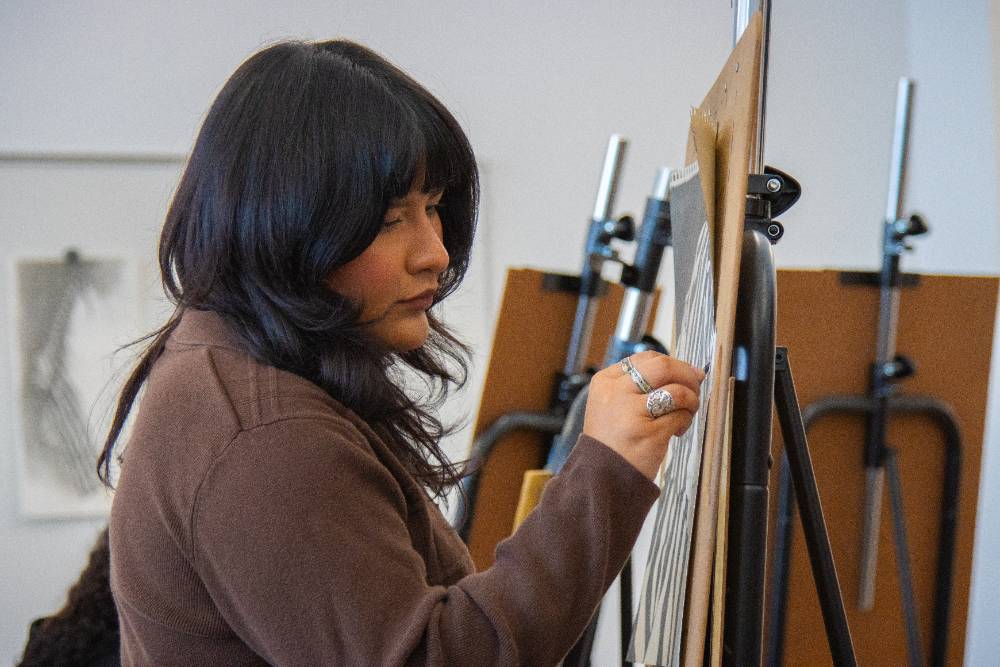 female student drawing on art easel