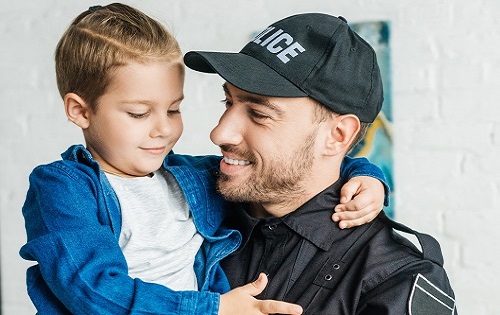 male police officer wearing ballcap holding small boy