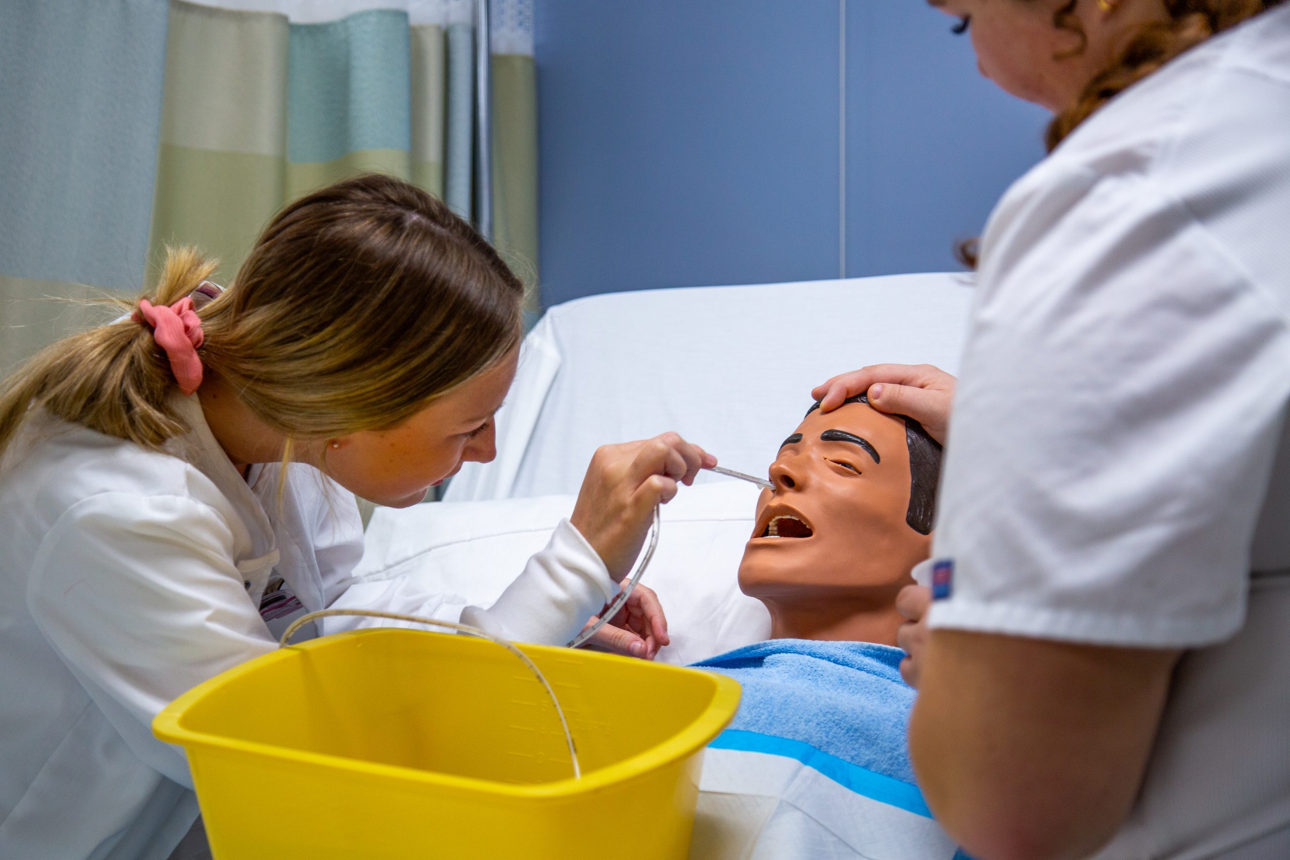 Two nursing students with a patient lying in bed, taking the patient's temperature.