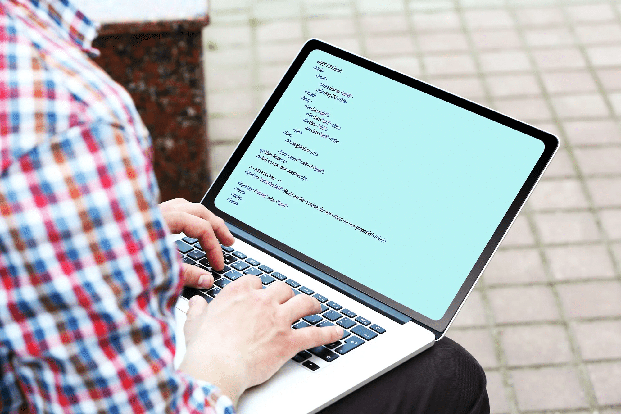 Man in a plaid shirt sitting with a laptop on his lap typing code