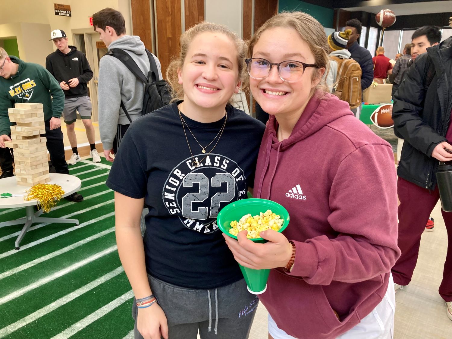 Students smiling at the camera holding a bucket of popcorn.