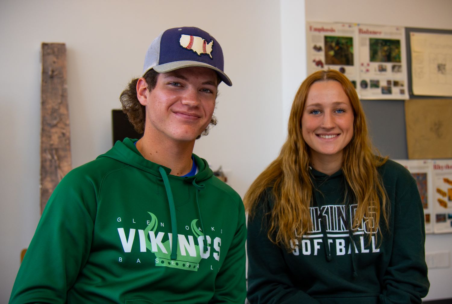 male student wearing Vikings baseball sweatshirt and baseball cap sitting next to female student wearing Vikings softball shirt